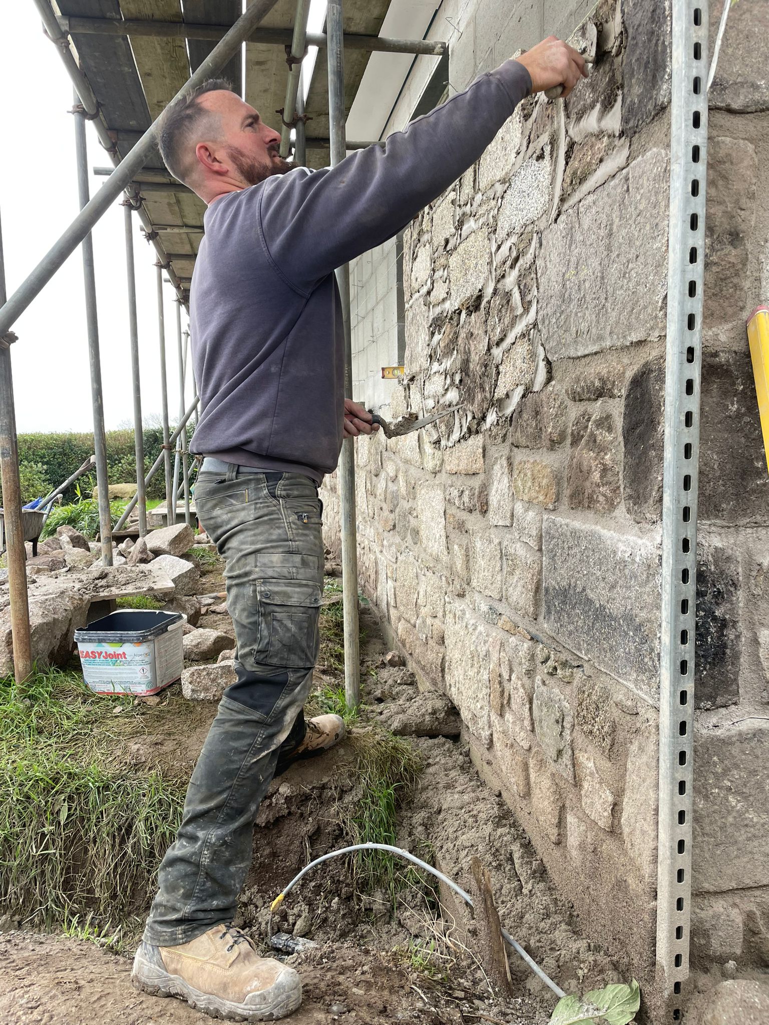 A member of the Bartlett Construction and Landscaping team working on an exterior stone wall at a property in West Cornwall